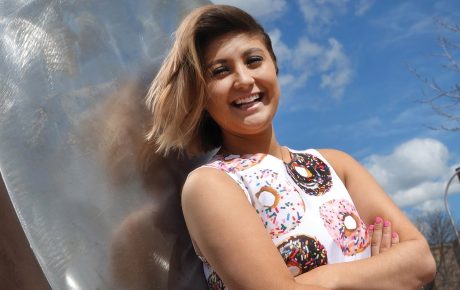 Photo of Rachael Cholak ’18 wearing a dress printed with donuts, in front of a large sculpture shaped like a donut.