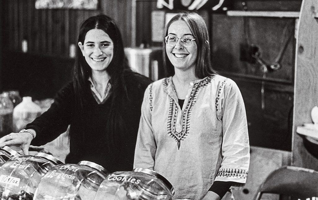 Image of Leslie Seeman and Barb Goldman standing behind the counter in the 1970's Brown University coffeeshop 