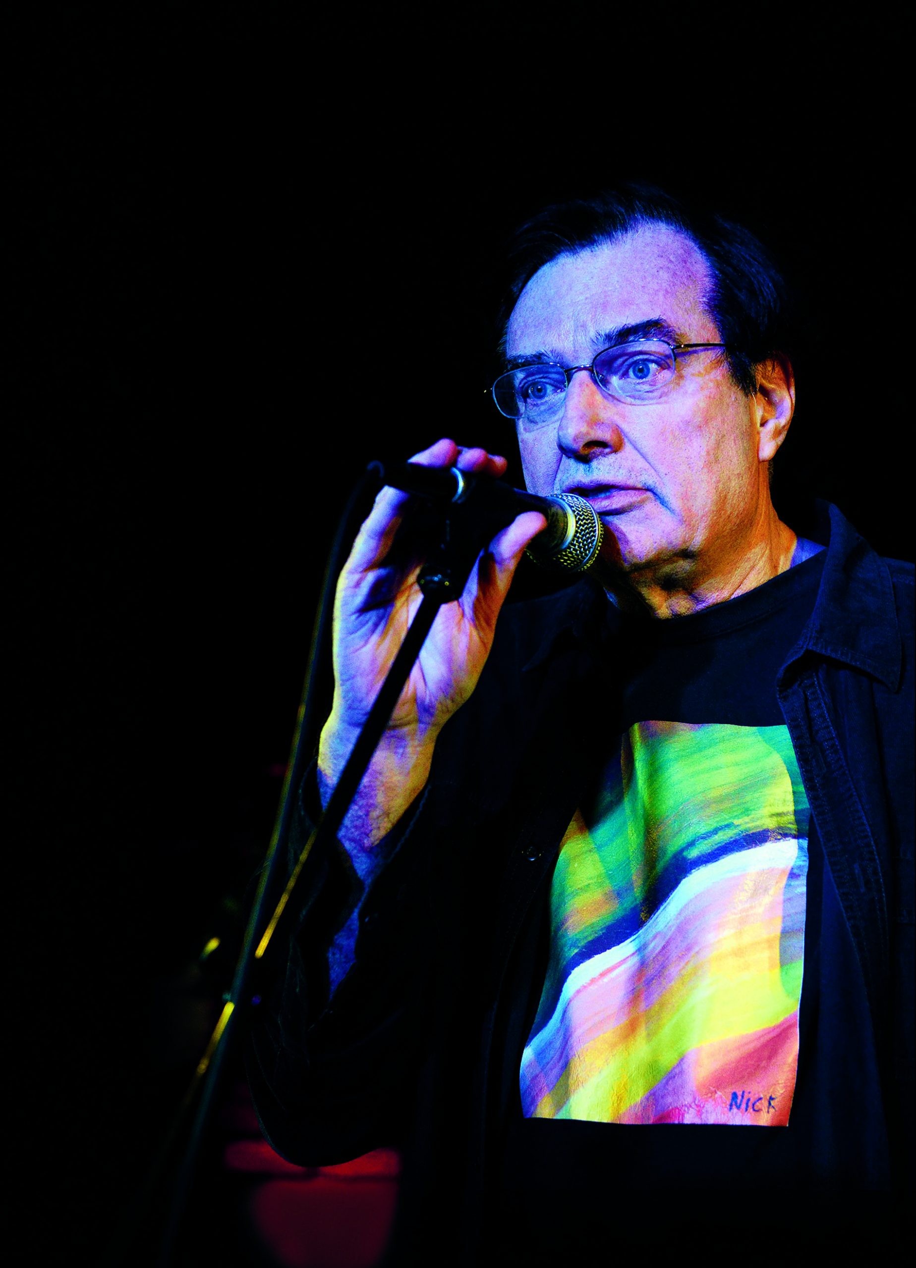 Close-up, dark image of Steve Morse speaking into a microphone.