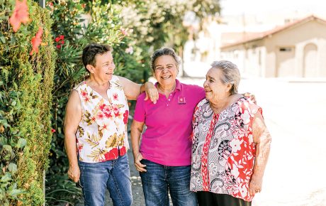 Three women standing in front of a botanical wall smiling.