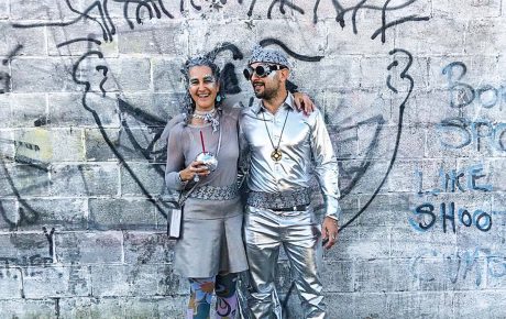 Monochromatic image of two people dressed in silver and grey with a grey background.