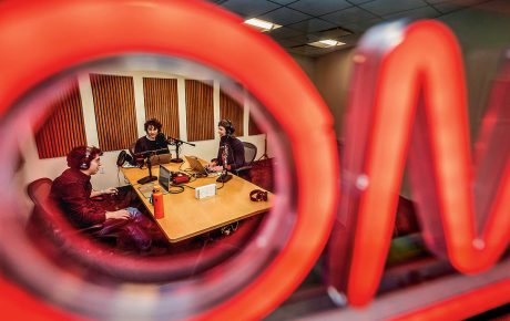 Image of students at a desk with laptops, microphones, and headphones.