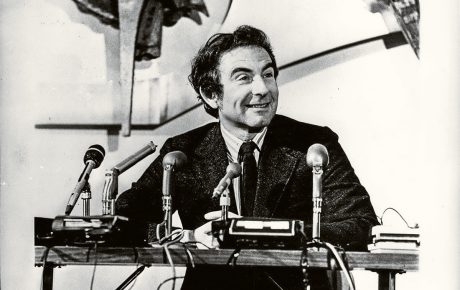 Archival image of Leon Cooper sitting at table with microphones in front of him.