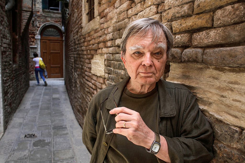 Image of Robert Coover leaning against a brick wall.