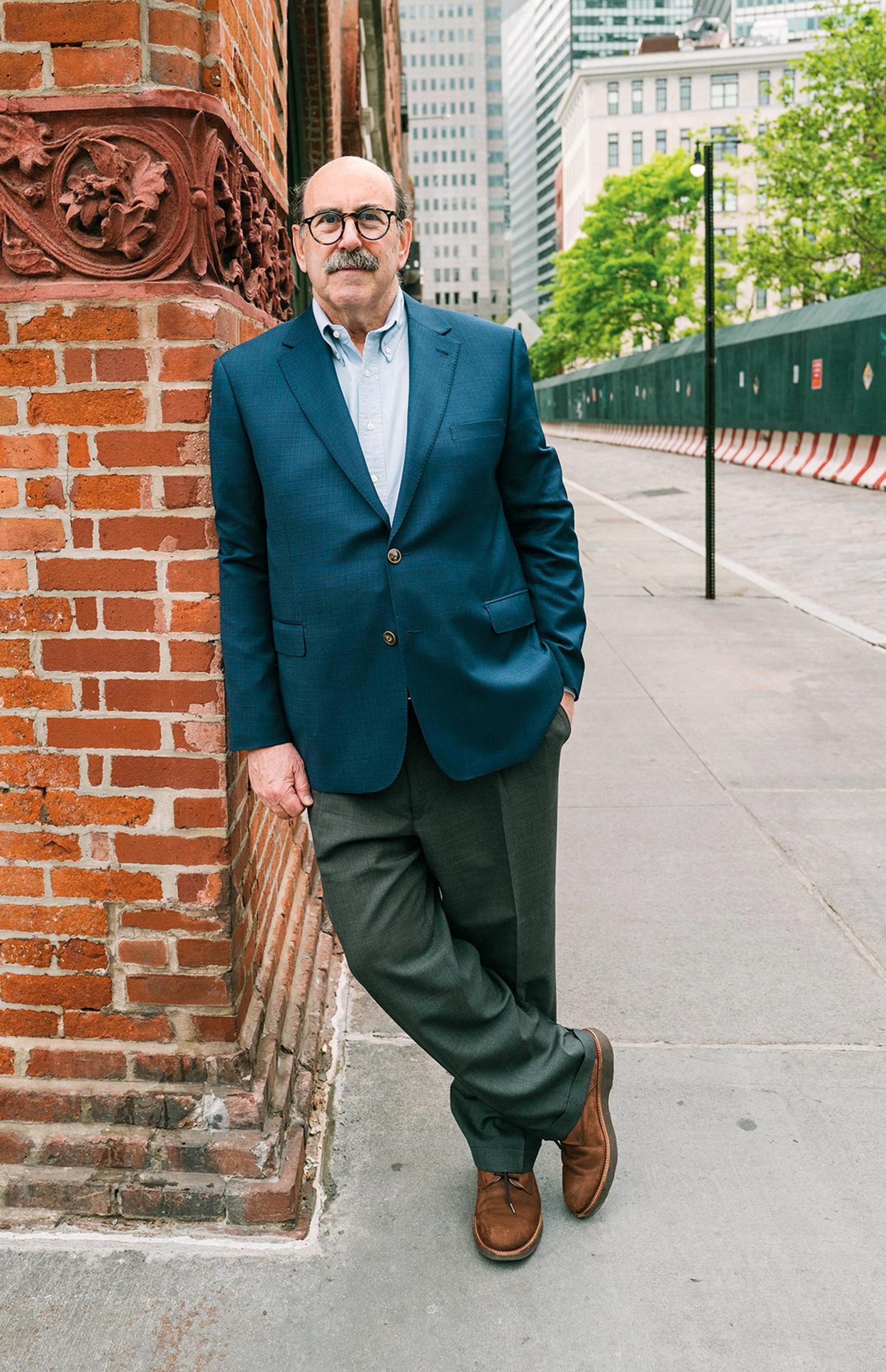 Image of Steve Cohen leaning against a brick pillar next to a street